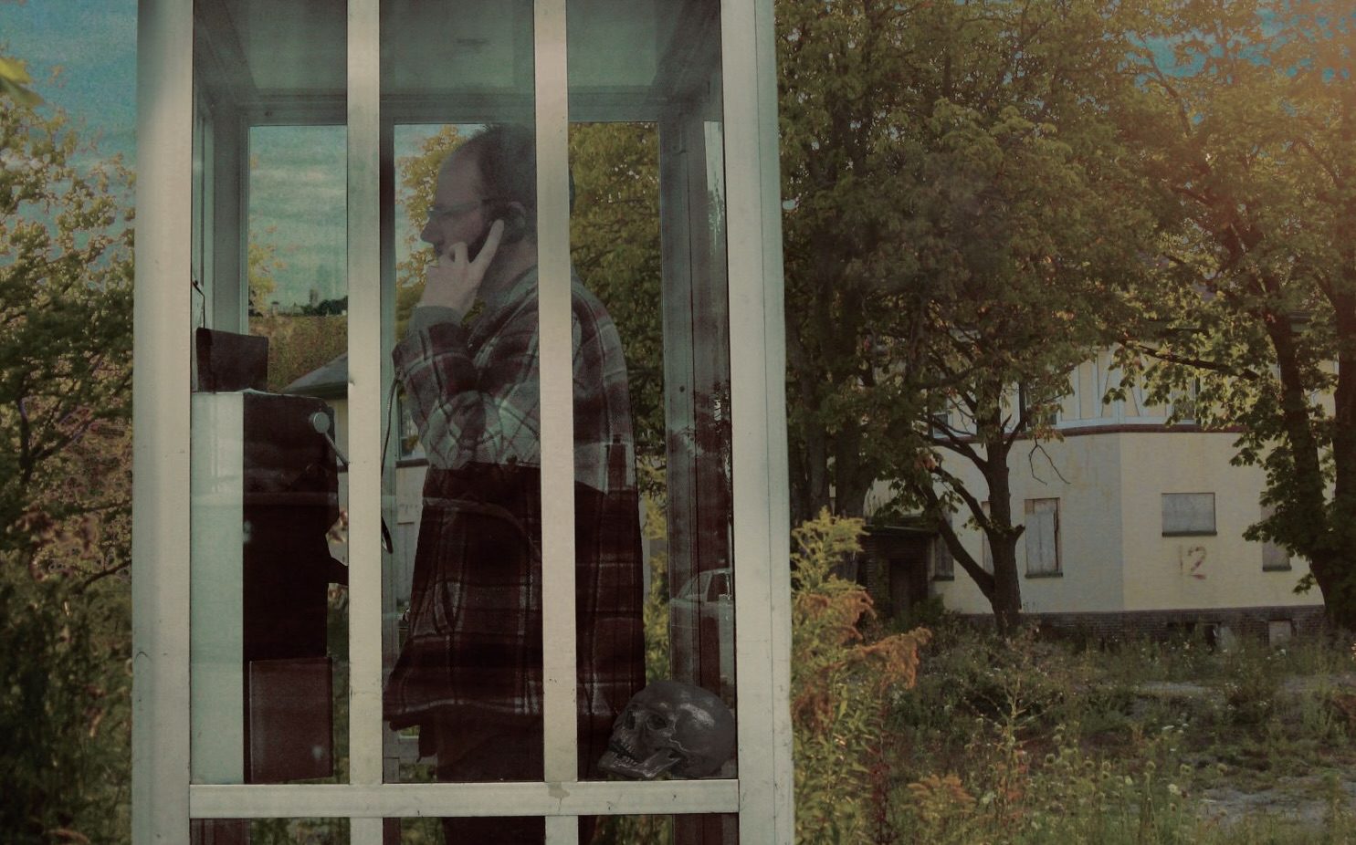 Black Schwartz standing in a glass phone booth with a skull resting nearby &ndash; promotional photo for Little Meadow